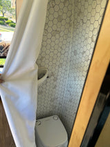Compact RV rental bathroom features white hexagon tiles, a Dometic toilet, and a shower curtain.