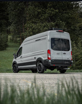 Light gray Venturhaus Ford Transit campervan, customized for adventure rv rental, parked by a forest.