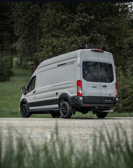 Light gray Venturhaus Ford Transit campervan, customized for adventure rv rental, parked by a forest.