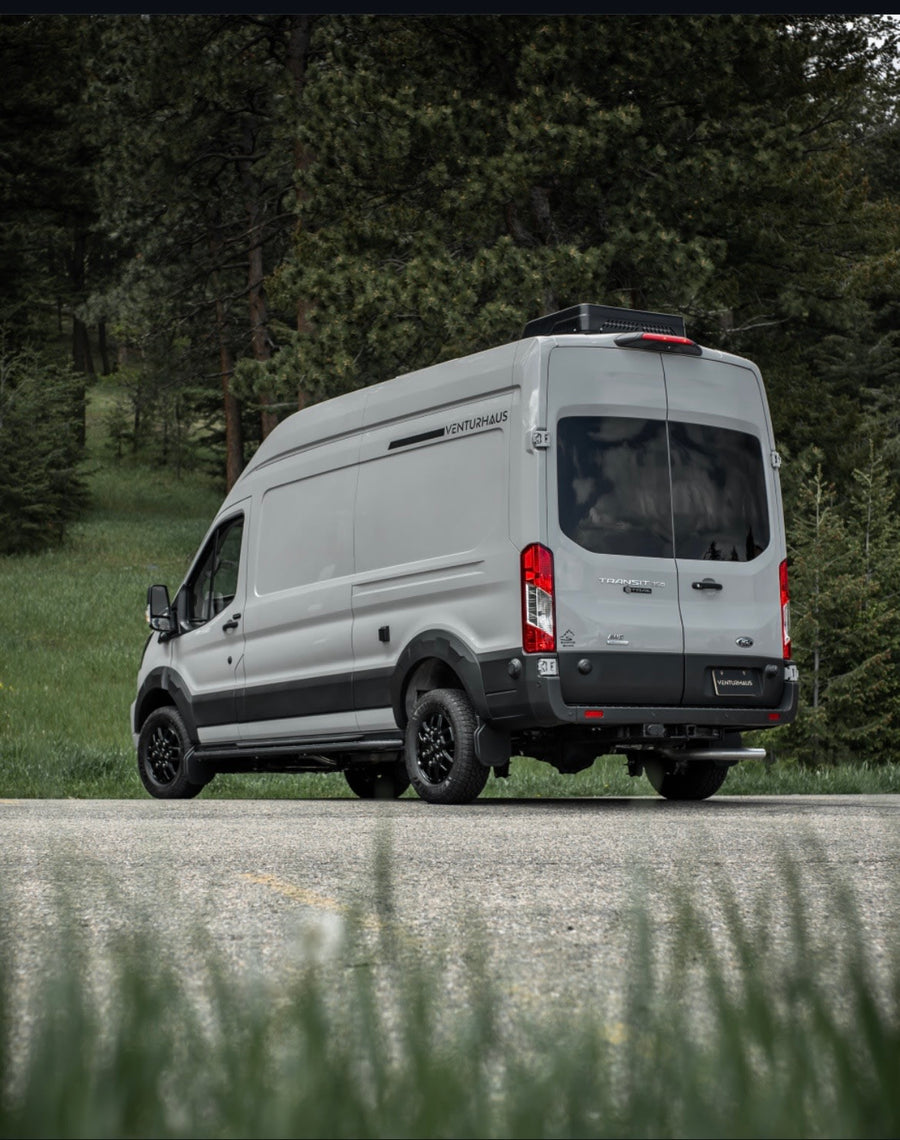 Light gray Venturhaus Ford Transit campervan, customized for adventure rv rental, parked by a forest.