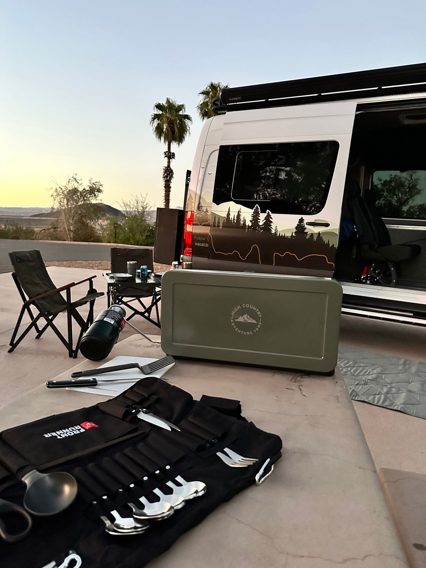 RV rental setup at sunset: A camper van with outdoor kitchen gear, chairs, & cutlery for desert adventures. — photo 7
