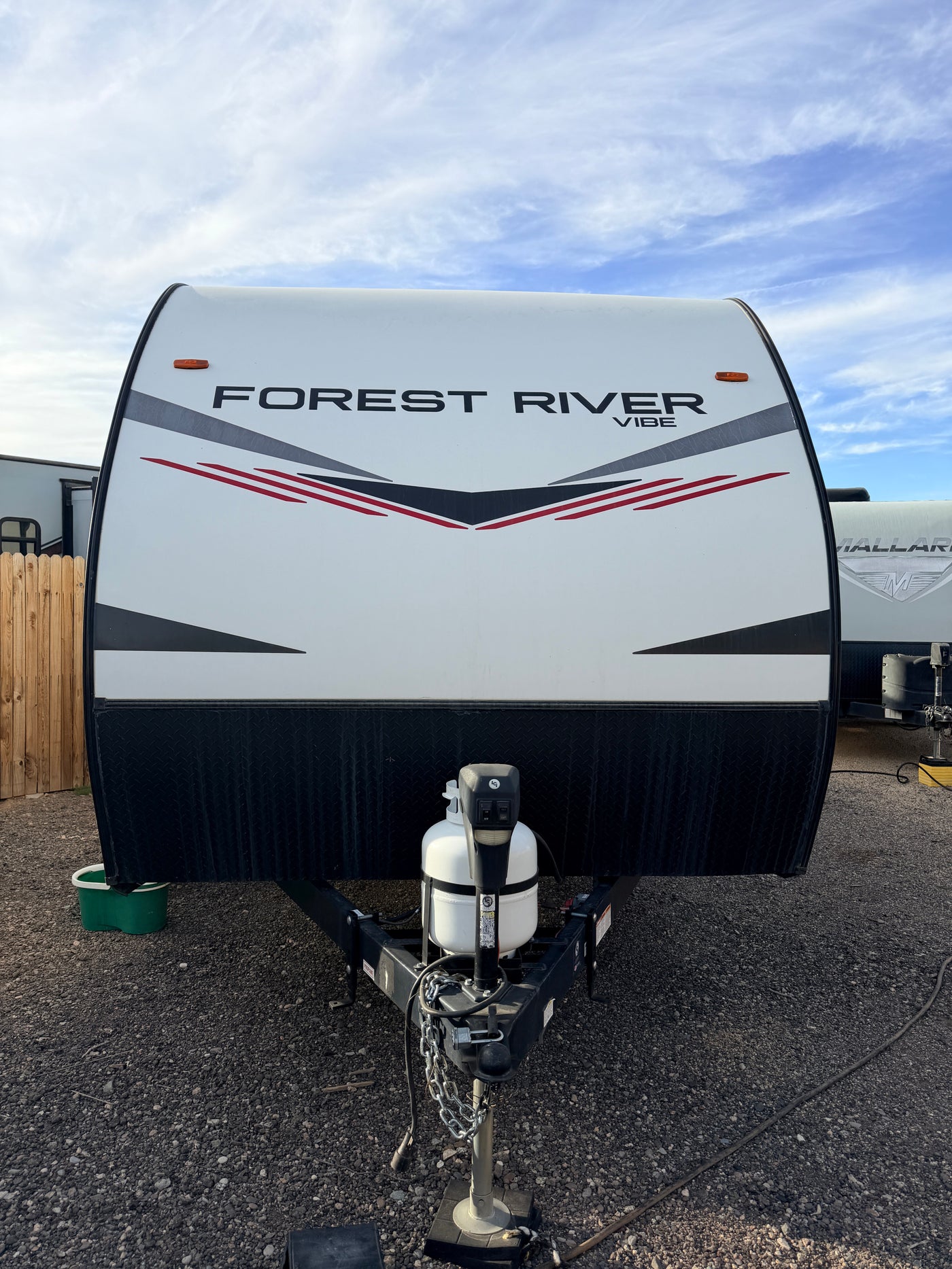White Forest River Vibe RV rental, front view. Shows propane tank, hitch on gravel, and a cloudy sky. — photo 13