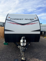 White Forest River Vibe RV rental, front view. Shows propane tank, hitch on gravel, and a cloudy sky.