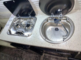 Compact rv rental kitchenette with a two-burner stove, sink, and open lids. Perfect for camper van cooking.