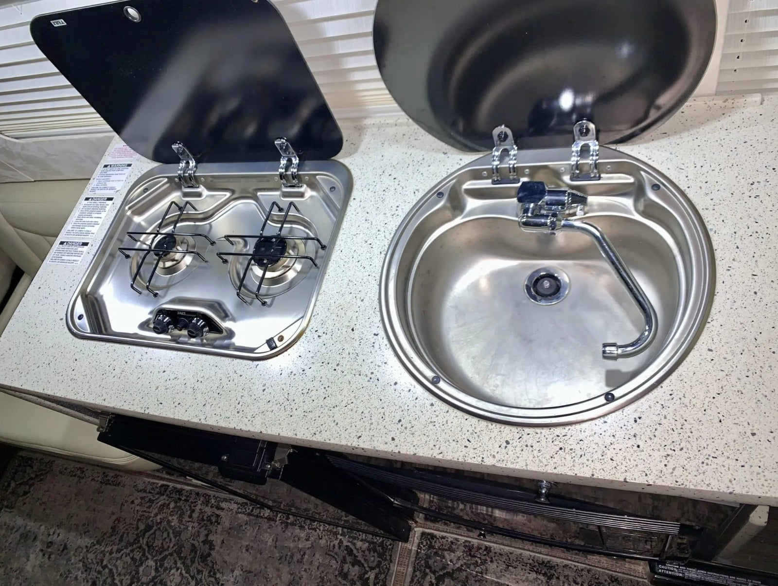 Compact rv rental kitchenette with a two-burner stove, sink, and open lids. Perfect for camper van cooking.
