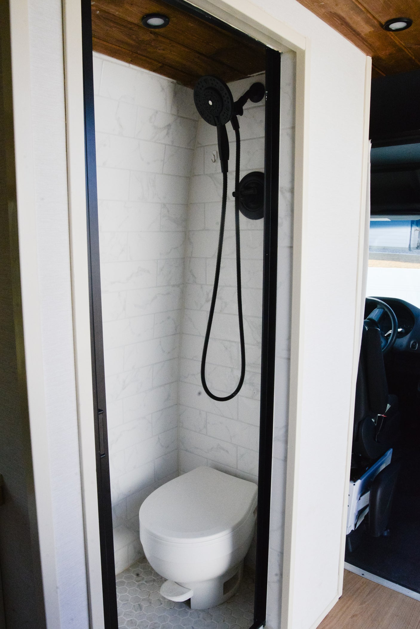 Compact RV rental bathroom with white subway tiles, a black shower, and toilet. Perfect for mobile living.