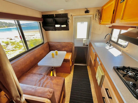 Inside an rv rental: inviting dining area & kitchen with a stunning coastal view outside the large window. Ready for adventure!