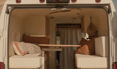 Cozy rv rental camper van interior with dual bench seating, decorative pillows, and a movable table setup.