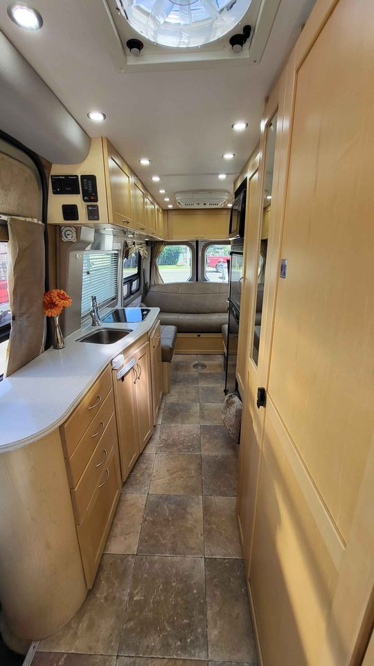  and clear dashboard. Ready for adventure!|Step into this RV rental van's front cab. Features tan swivel captain's chairs — photo 7