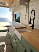 Stunning RV rental interior: modern kitchen with farmhouse sink, black faucet, wood counters, & breathtaking ocean view.