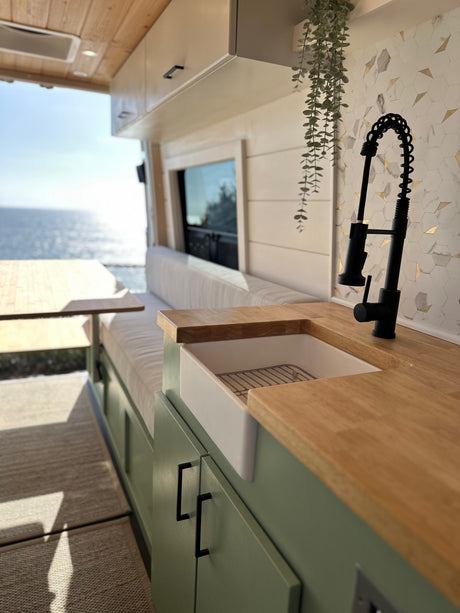 Stunning RV rental interior: modern kitchen with farmhouse sink, black faucet, wood counters, & breathtaking ocean view.