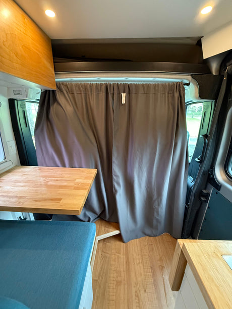 Cozy RV rental interior: wooden table, blue cushion, and privacy curtains for the cabin area.
