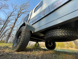 Low-angle view of an off-road camper trailer, perfect for your next RV rental adventure. Parked by a lake with trees.