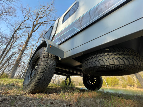Low-angle view of an off-road camper trailer, perfect for your next RV rental adventure. Parked by a lake with trees.