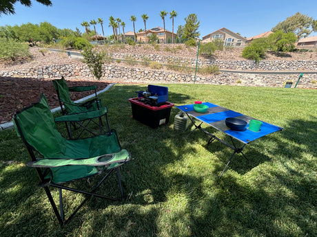Backyard picnic setup: two green chairs, portable stove, and table on grass. Great for outdoor living after an RV rental adventure.