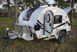White "Boondock" **teardrop RV rental** with off-road features, open door, storage. Parked on grass, adventure-ready.