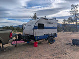 RV rental camping setup: Sunray Sport travel trailer with a truck in a rustic mountain setting under a cloudy sky.