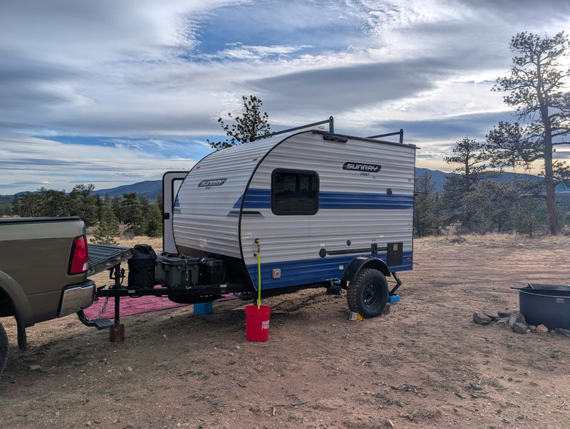 RV rental camping setup: Sunray Sport travel trailer with a truck in a rustic mountain setting under a cloudy sky. — photo 7