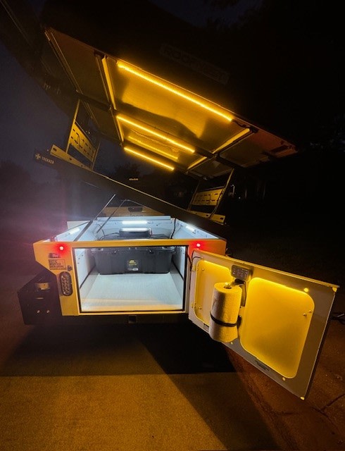 Brightly lit rv rental adventure trailer at night, showing open storage and overhead LEDs, ready for any journey.