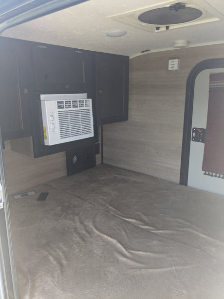 Compact RV rental interior with Frigidaire AC, dark cabinets, and a soft mattress for a cozy stay.