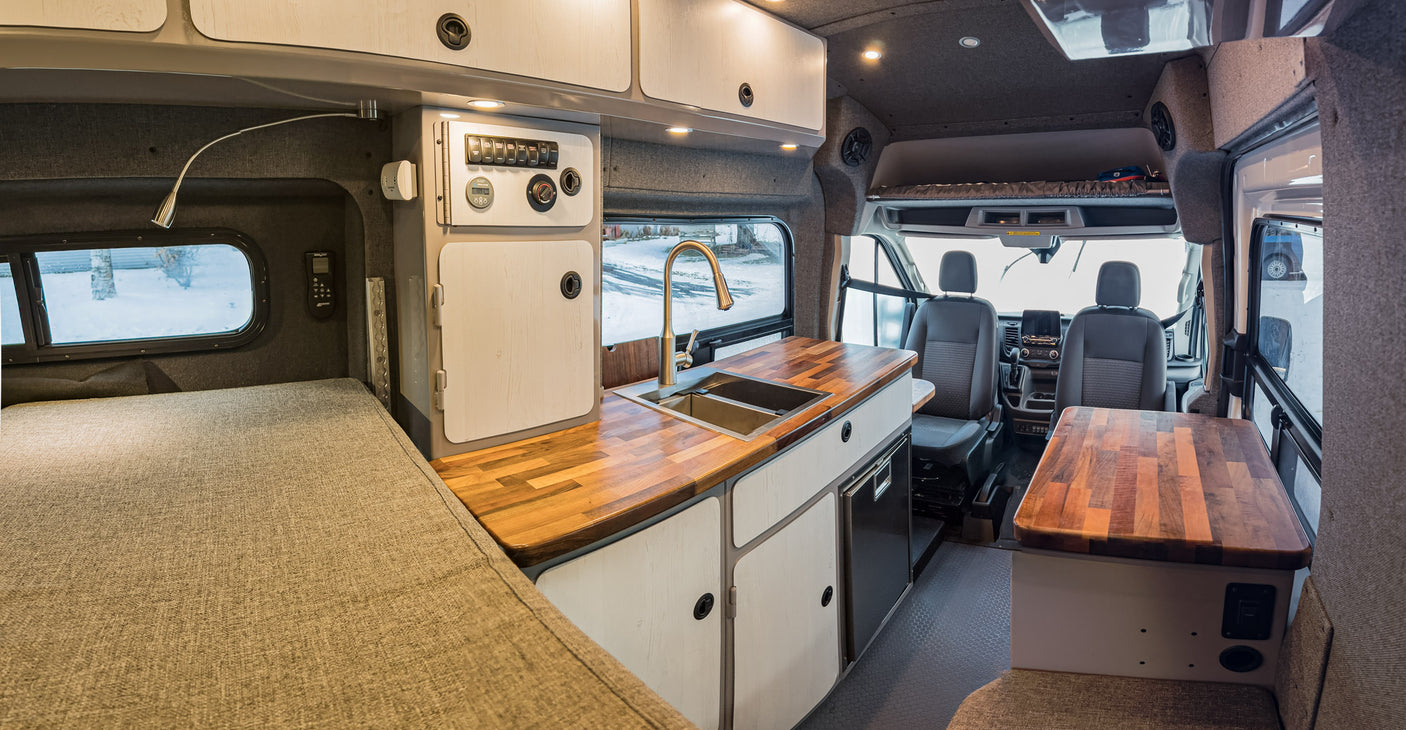 Cozy RV rental interior featuring a full bed, modern kitchenette, and convertible living space for comfortable travels.