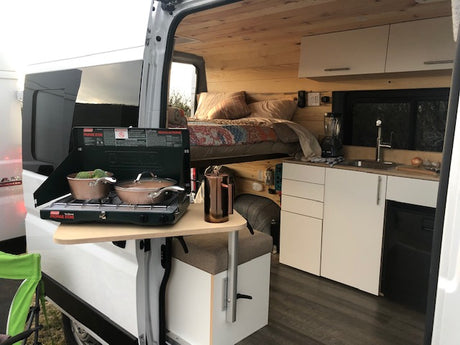 This rv rental features a cozy interior with a built-in kitchen, elevated bed, and outdoor propane stove setup for versatile camping.