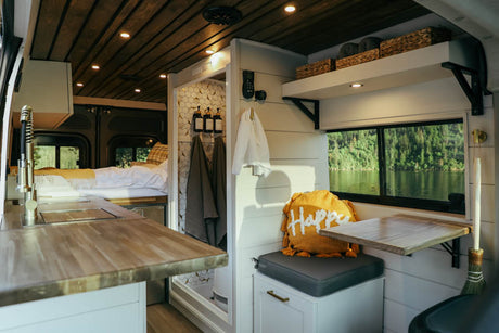 Explore this cozy rv rental interior with a functional kitchen, bed, shower, and serene lake views.