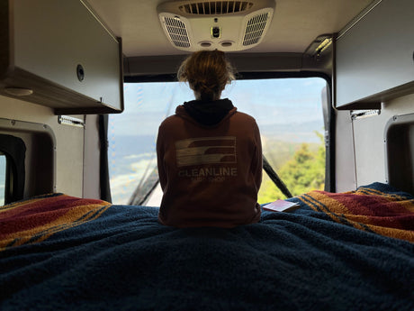 Inside a comfy RV rental, a person looks out the back window at a scenic view from their bed. Overhead cabinets are visible.