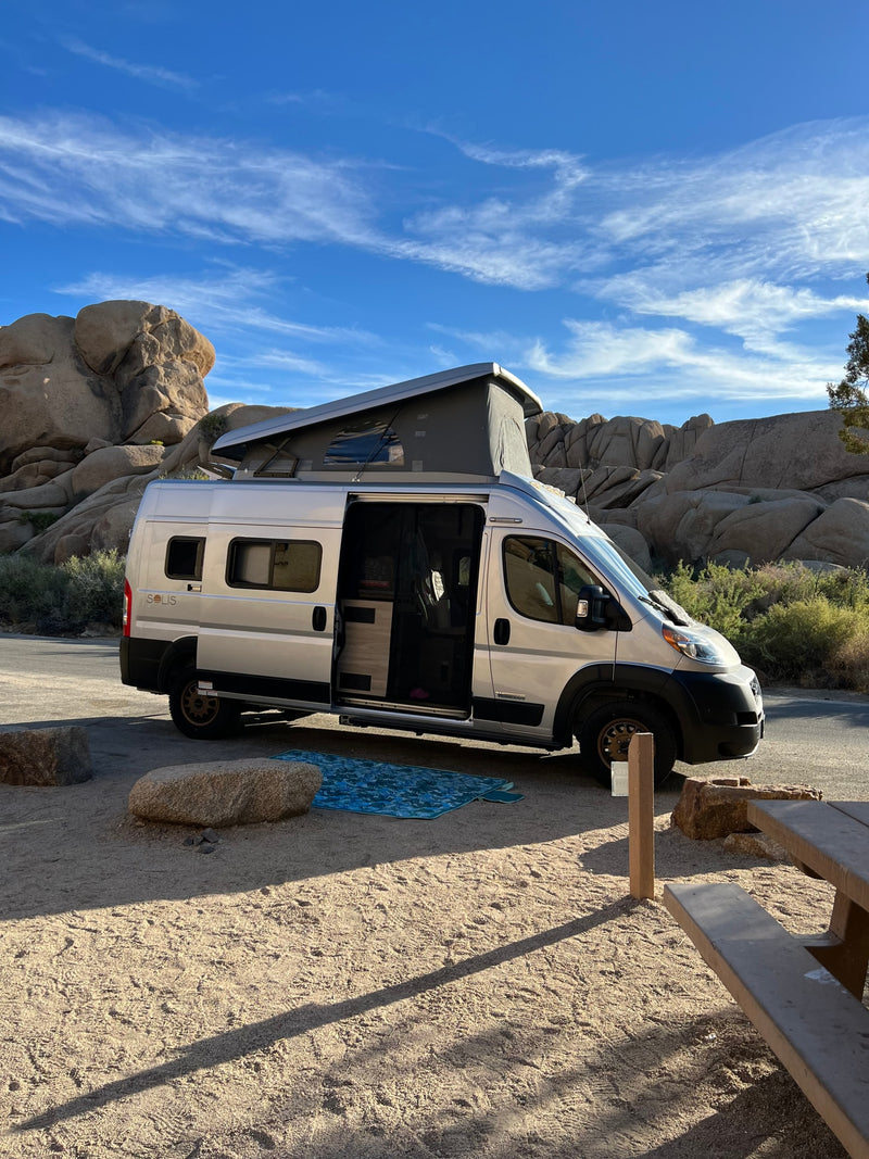 An RV rental pop-top camper van is parked at a sunny, rocky desert campsite. Its side door is open, revealing the interior. — photo 10