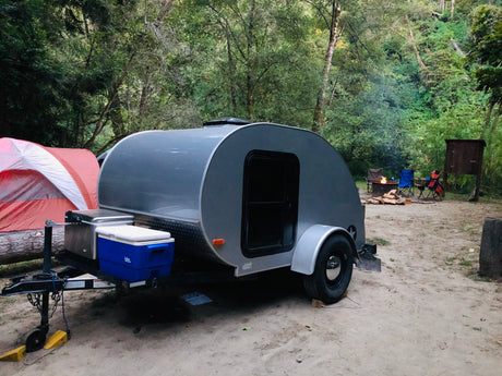 Experience outdoor travel with an RV rental. A small RV, tent, and campfire are ready at a scenic campsite.