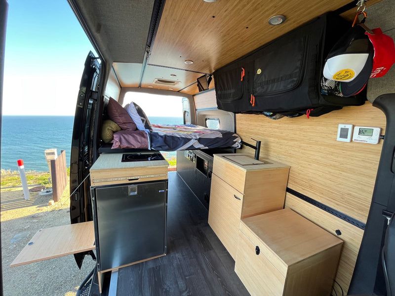 This RV rental interior offers an ocean view from its comfortable bed, alongside a full kitchenette and smart storage. — photo 2