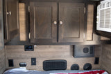 RV rental interior featuring dark wood cabinets, AC unit, control panel, outlets, and vents above a striped bed.