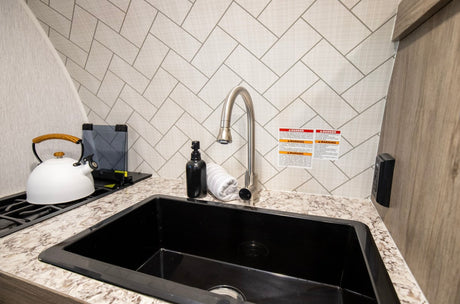 An RV rental's compact kitchen with a black sink, sleek faucet, herringbone patterned backsplash, and stovetop kettle.