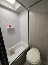 Clean RV rental bathroom with a white herringbone shower, bathtub, toilet, and wood-look walls. Features a skylight.
