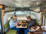 Couple dines in a functional RV rental. Built-in bed, seating, and clever storage maximize space.