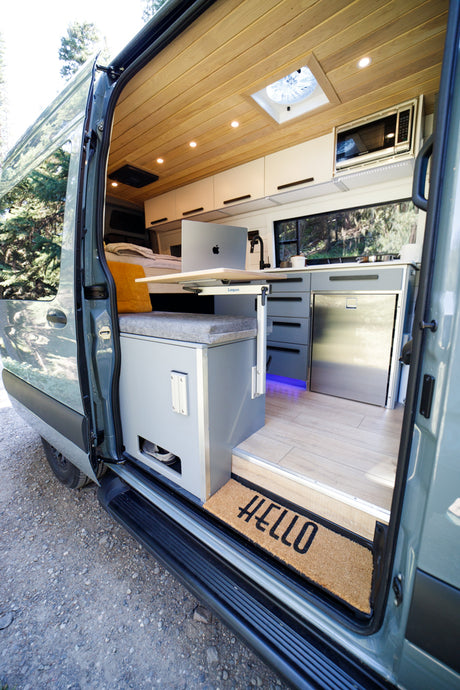 RV rental: Modern camper van interior with wood ceiling, laptop desk, kitchen, and cozy bench.