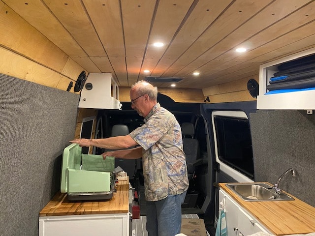 Comfortable RV rental: Man setting up a portable grill in a customized camper van kitchen. — photo 13