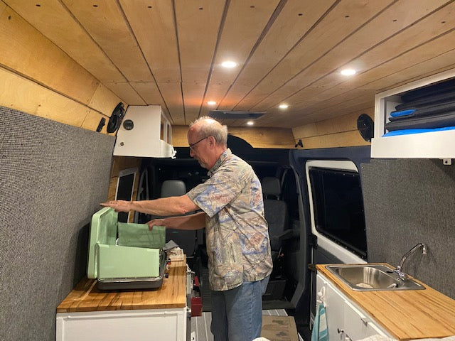 Comfortable RV rental: Man setting up a portable grill in a customized camper van kitchen.