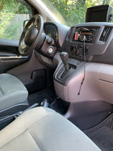 Inside a compact Nissan cargo van, potentially an RV rental base, showing the dashboard, steering wheel, and automatic shifter.