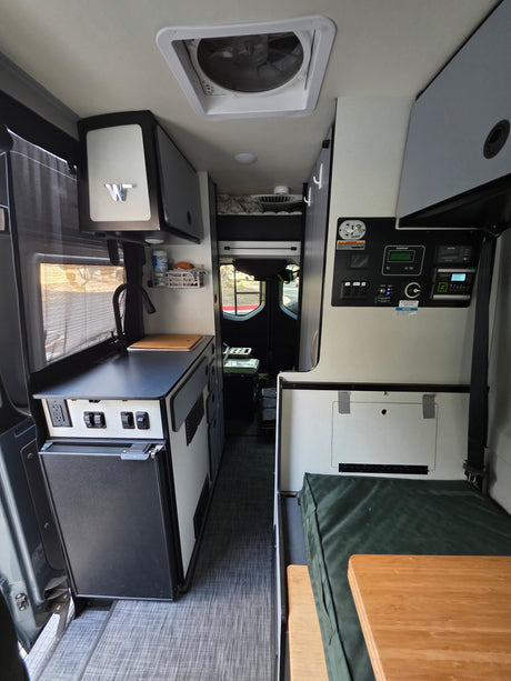 Inside an RV rental: full kitchen with fridge, central control panel, and a cozy bench/table living space. Ready for adventure.