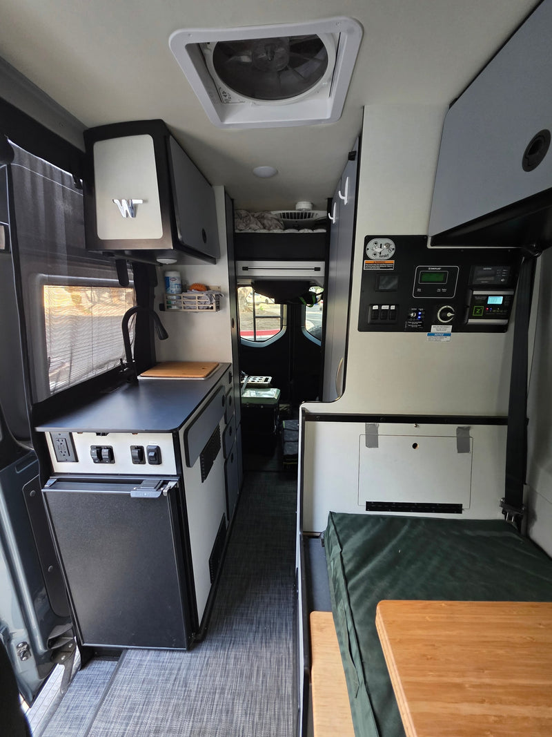 Inside an RV rental: full kitchen with fridge, central control panel, and a cozy bench/table living space. Ready for adventure. — photo 10