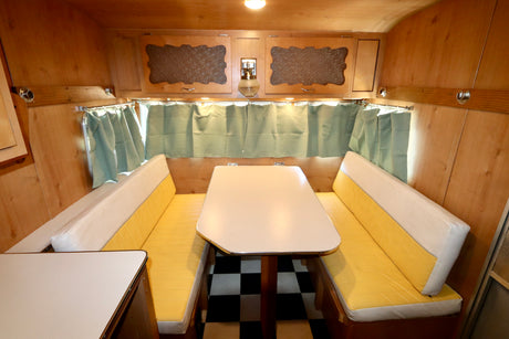 Cozy vintage RV rental interior: wood-paneled dinette with yellow and white cushions, classic checkerboard floor.