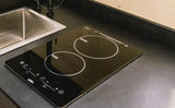 Modern RV rental kitchen features a built-in induction cooktop and stainless steel sink on a dark countertop.