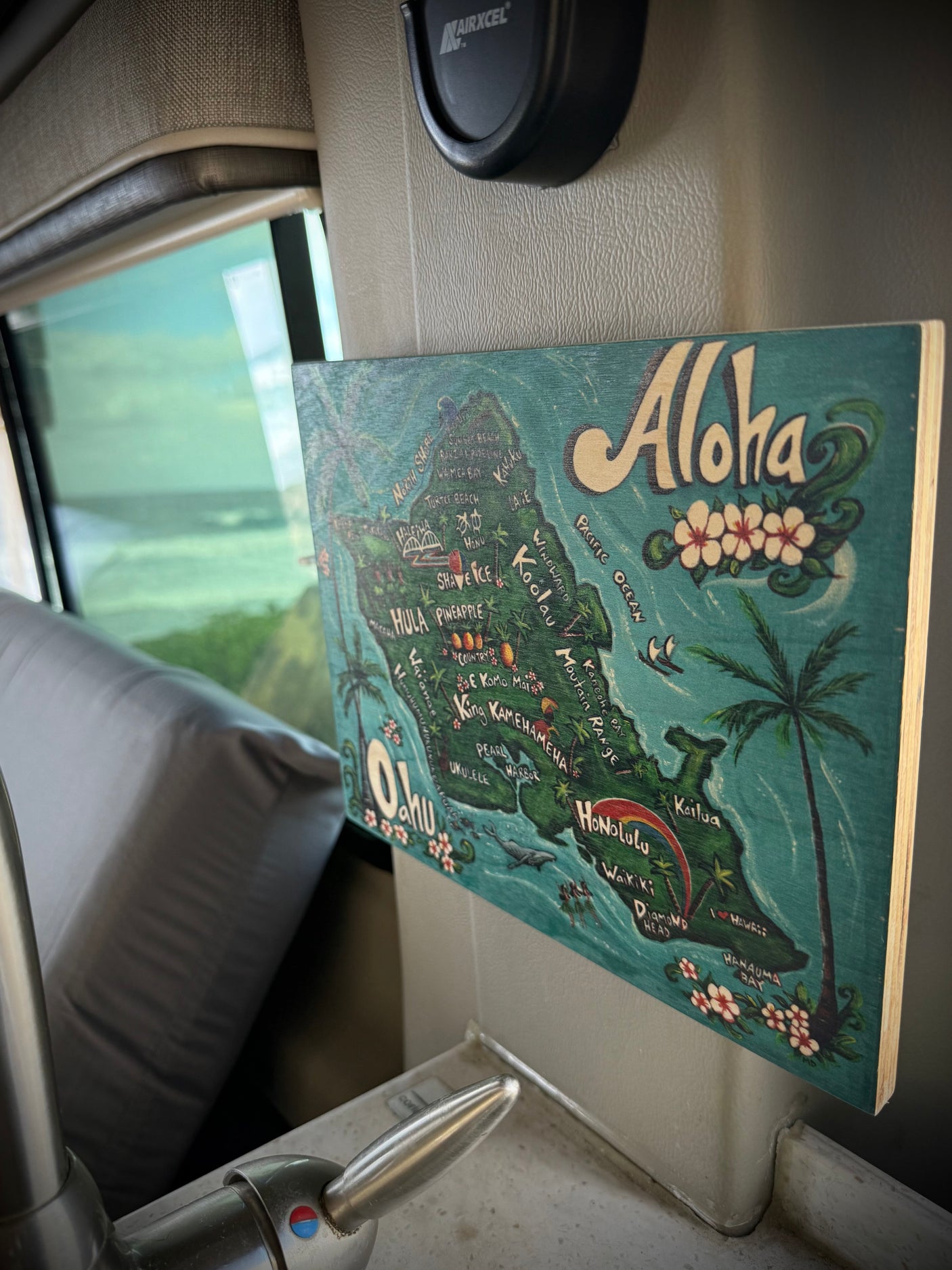 RV rental interior with an "Aloha" Oahu map, sink, and a scenic ocean view out the window, suggesting a travel adventure.
