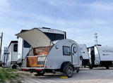 This grey teardrop camper with an open outdoor kitchen offers compact RV rental adventures, parked alongside other travel trailers.