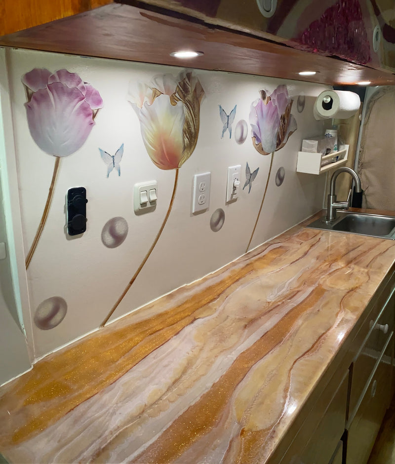Custom RV rental kitchenette with a glitter epoxy counter, sink, and whimsical floral wall decor accented by LED task lighting. — photo 12