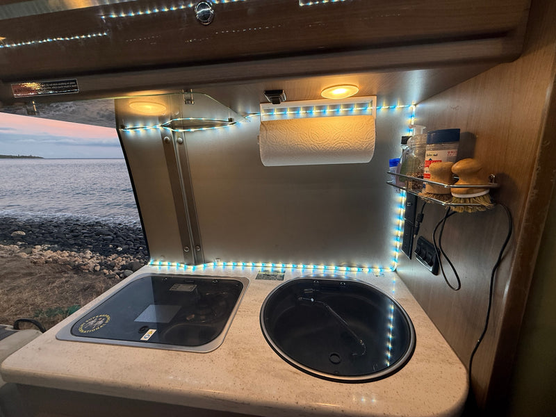 An RV rental kitchen with a stovetop, sink, and view of the ocean, illuminated by LED lights. — photo 14