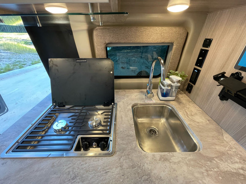 Compact RV rental kitchen features a two-burner stove, sink, and useful counter space with window view. — photo 11