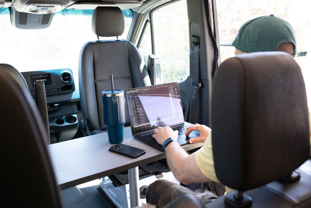 Inside an RV rental van, a person works on a laptop at a table, highlighting a comfortable mobile office.