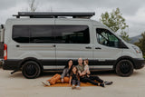 Smiling family of four on a blanket by a white camper van, ideal for an RV rental outdoor adventure.